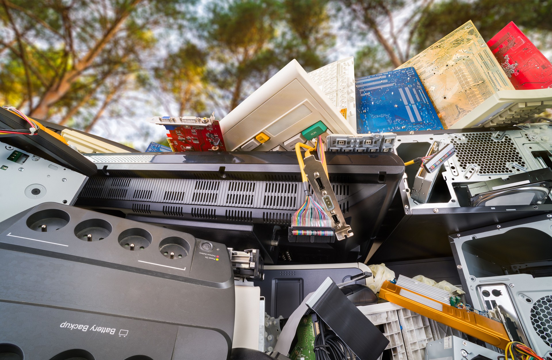 Electronic waste detail. Discarded computer hardware components on pile under trees with sunny sky